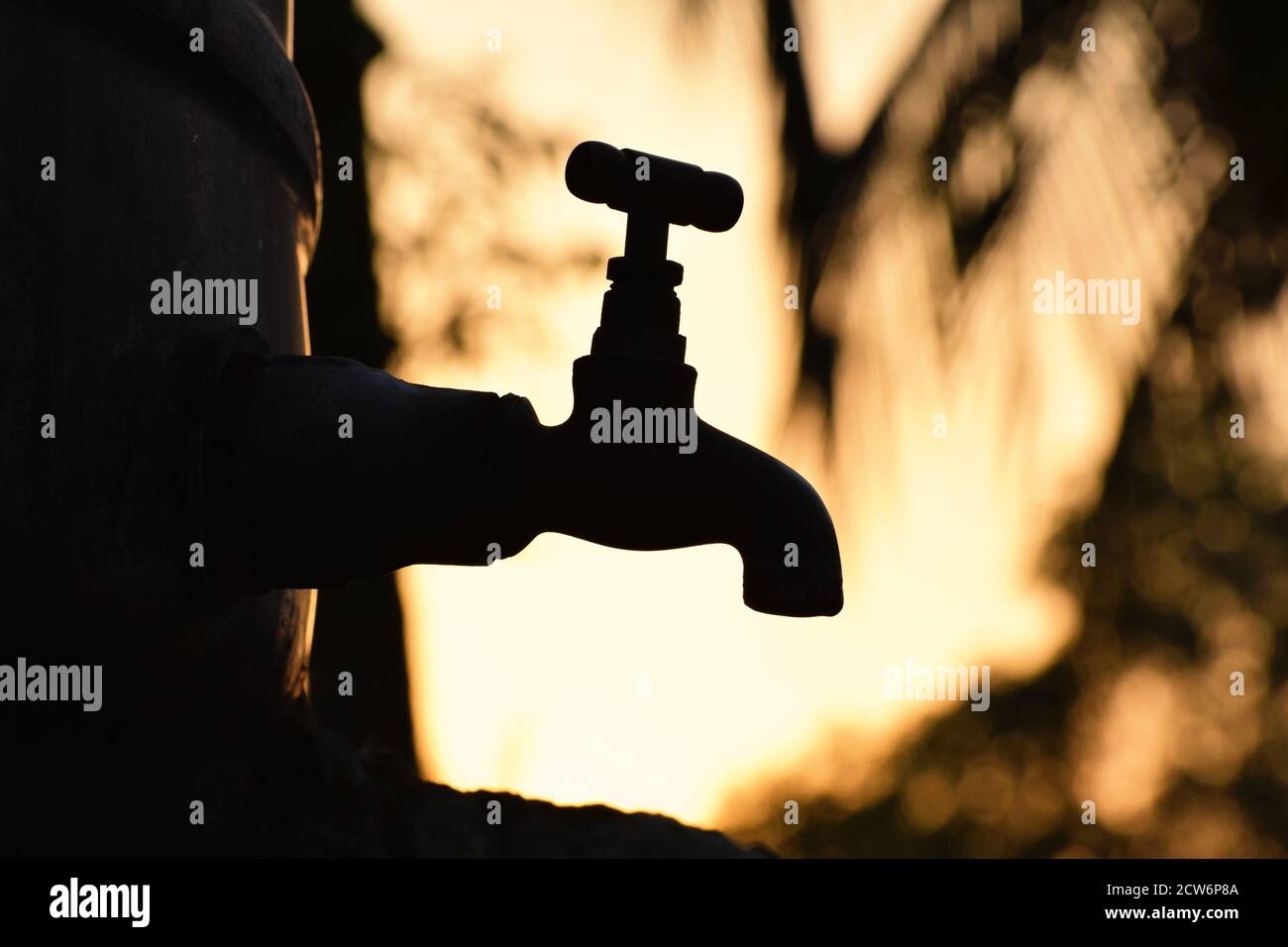 Silhouette of old vintage metal faucet/tap alone in an outdoor natural environment during golden hour of sunrise, water shortage, beautiful wallpaper Stock Photo