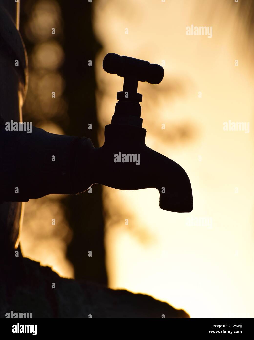 vertical / portrait-oriented Silhouette of old vintage metal tap alone in outdoor natural dry environment during golden hour, water shortage, drought Stock Photo