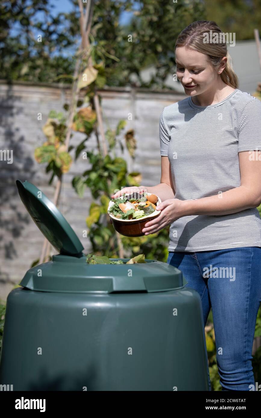 Woman Emptying Food Waste Into Garden Composter At Home Stock Photo