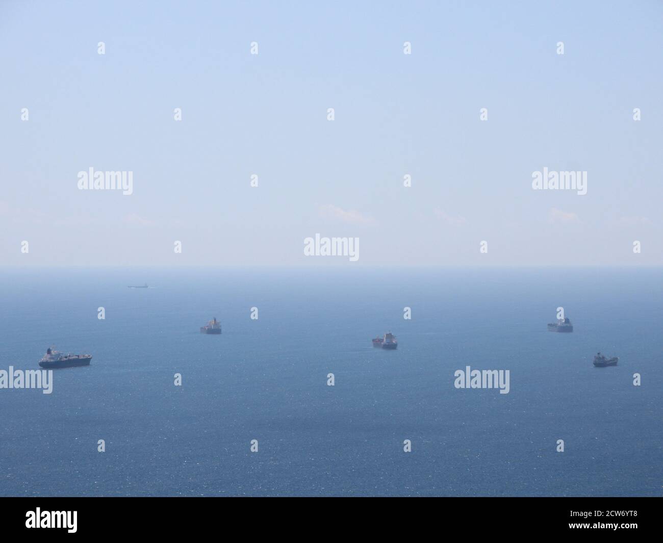Five industrial container ships waiting at open sea. The ocean is blue and the horizon looks foggy. Stock Photo