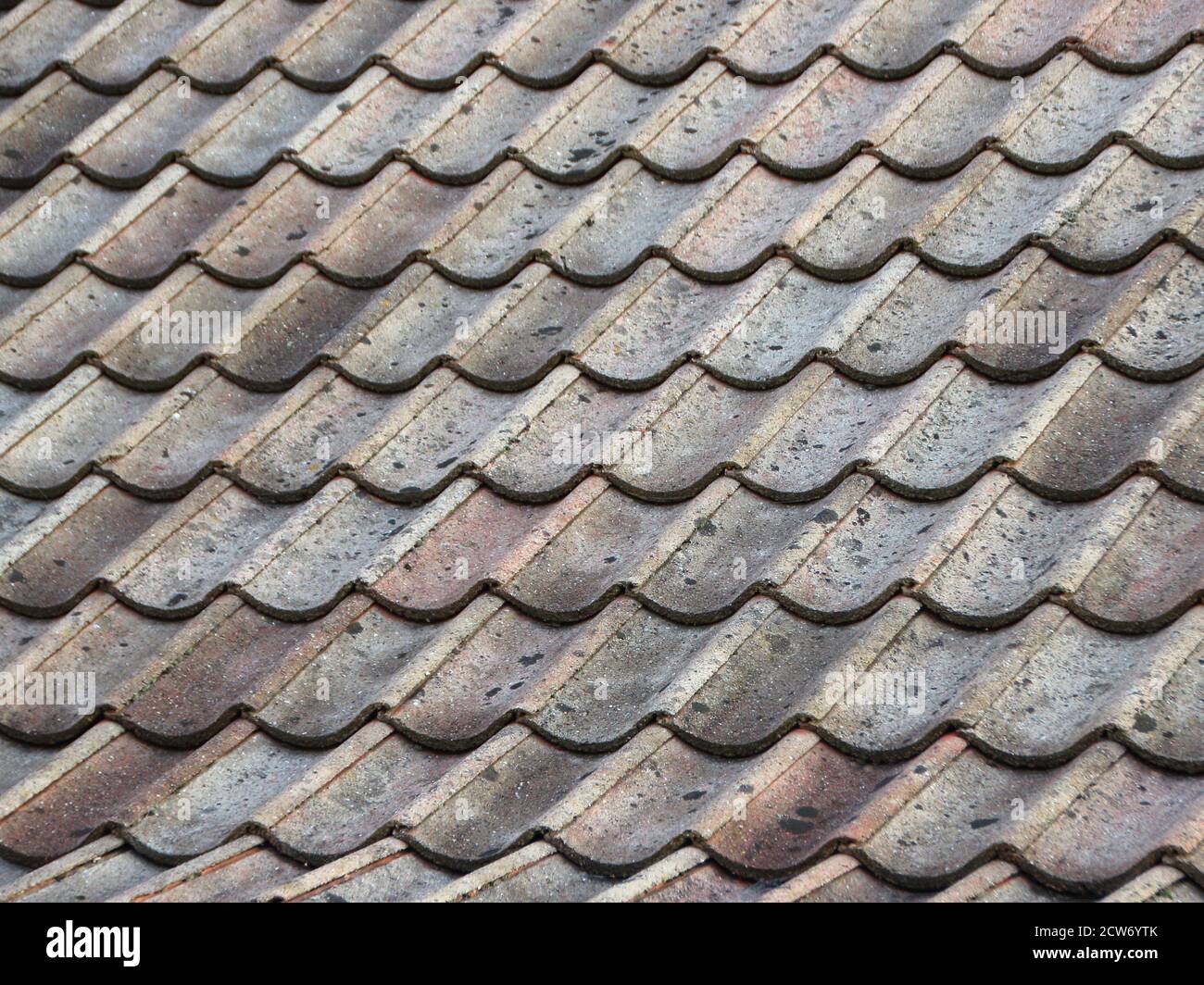 Worn cement roof tiles seen from a slanted angle. The colors are muted and only the roof of the house is seen. Stock Photo