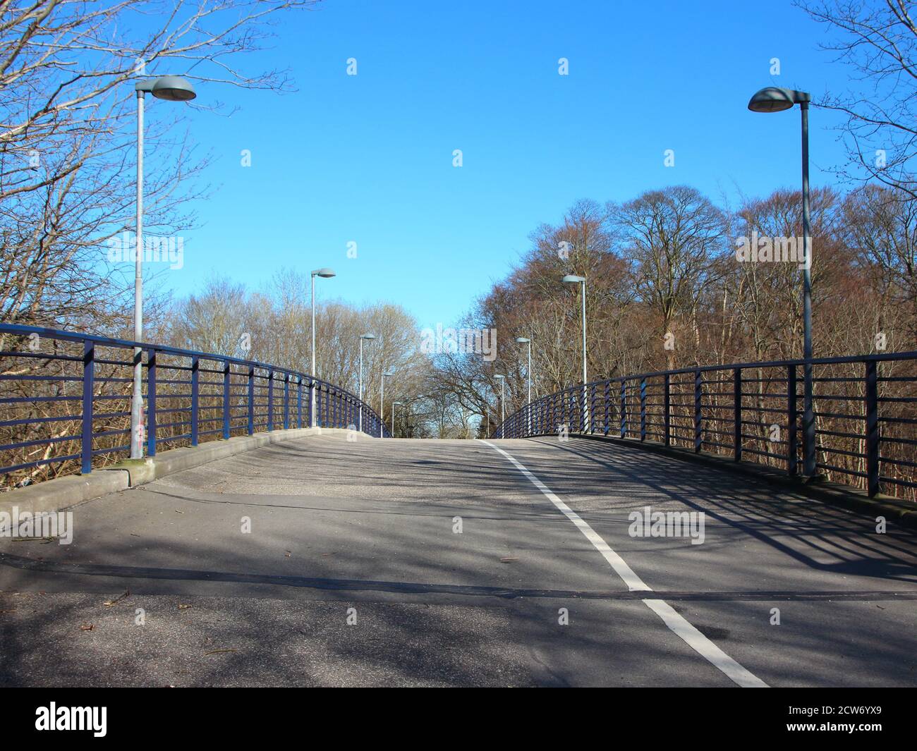 An empty curved pedestrian and bicycle crossing road. It is a bridge with lampposts on either side. Stock Photo