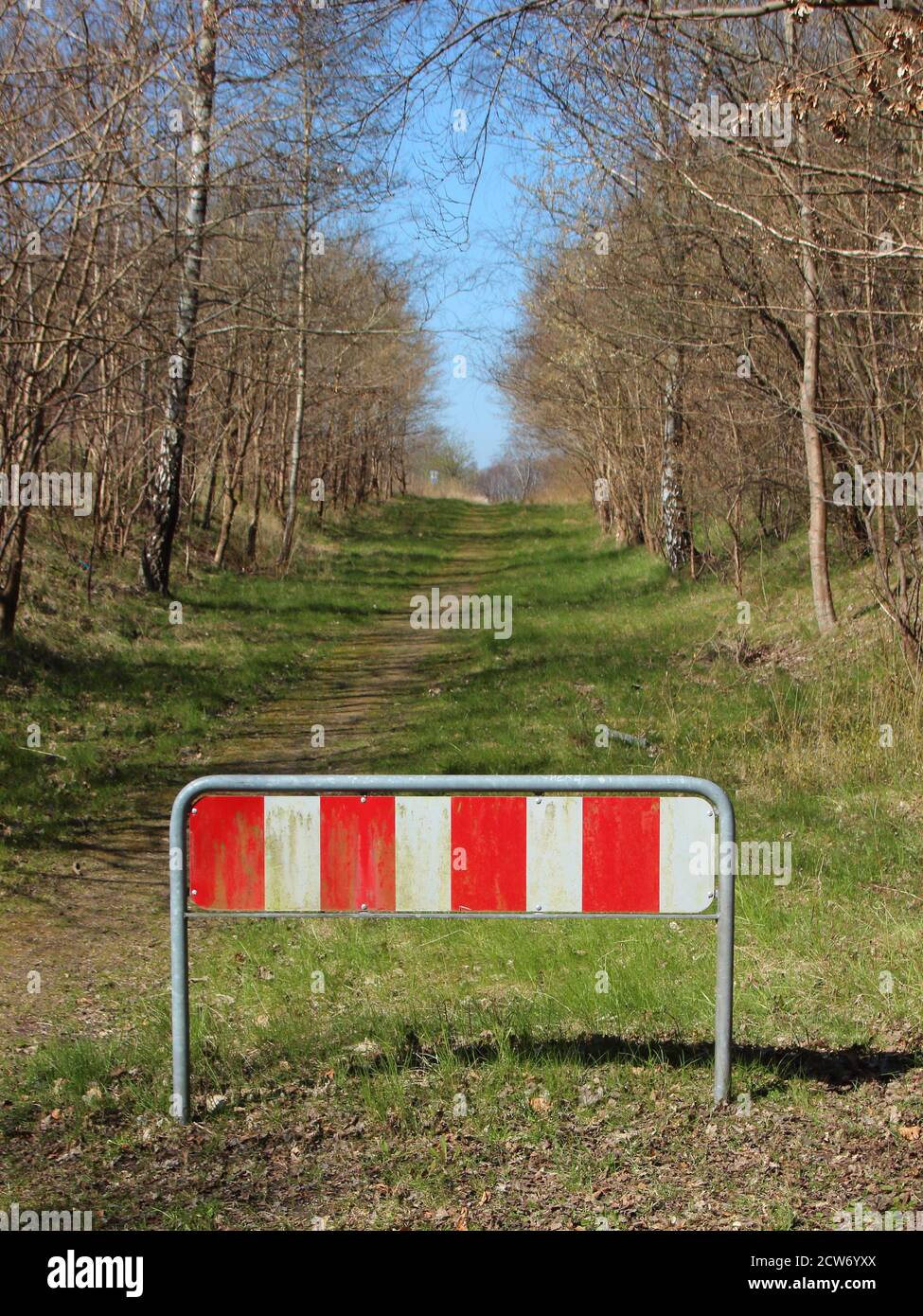 A road end sign with red and white stripes, surrounded by trees on both sides. Stock Photo