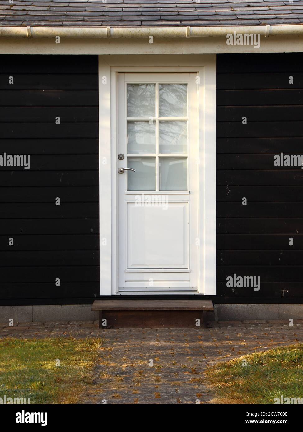 An isolated white door contrasting with a classic scandinavian black wooden house, shot vertically. Stock Photo
