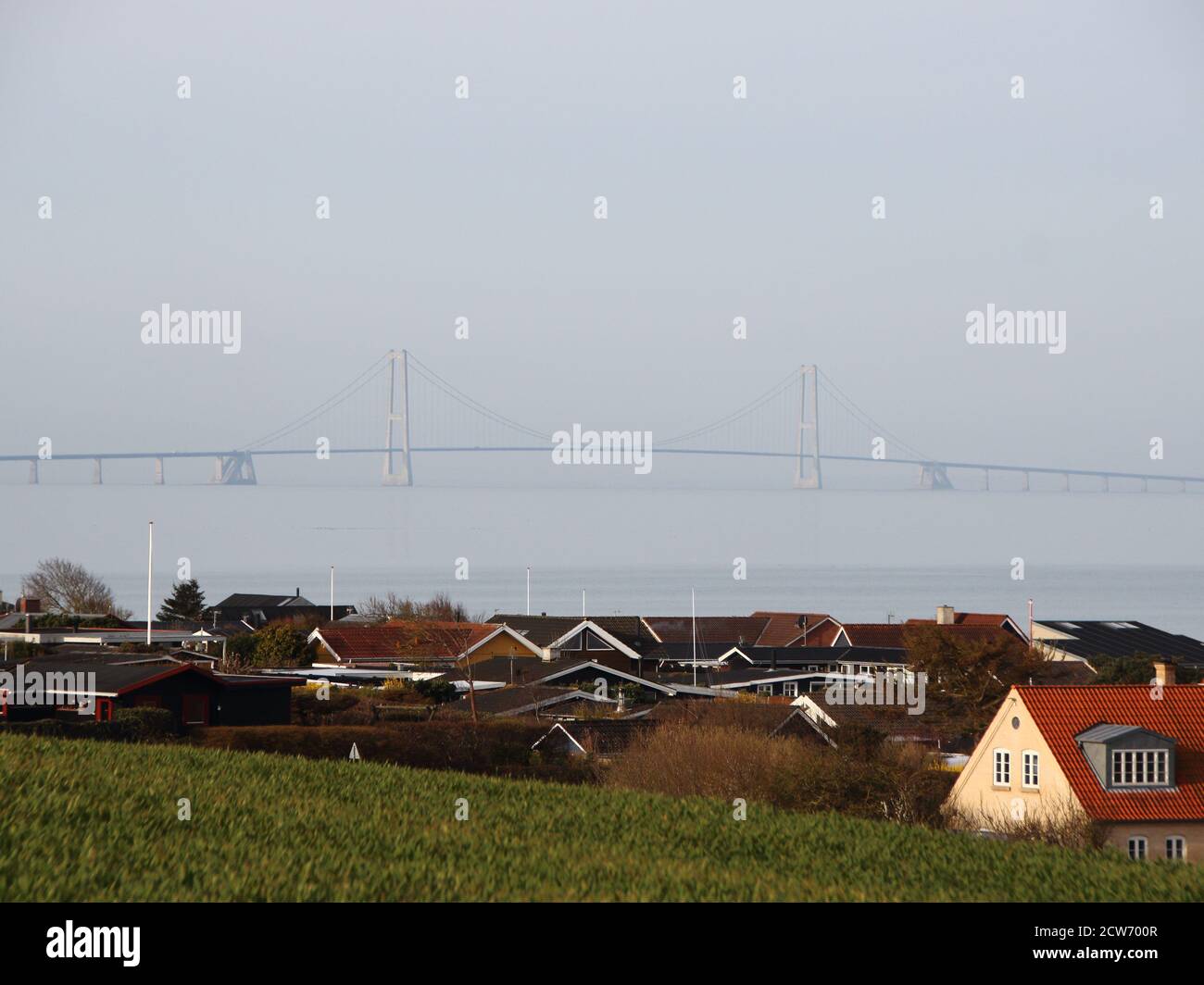 A bridge over a large danish body of water in heavy fog. The bridge can be seen through the fog in the background, whilst the rooftops of different ho Stock Photo