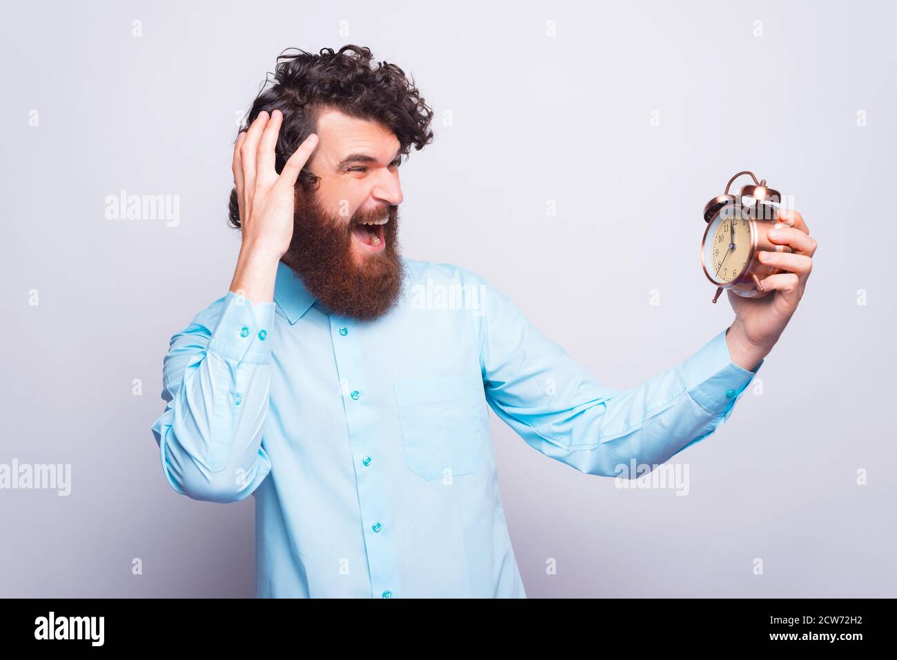 What is the hour, bearded man in casual looking afraid at alarm clock