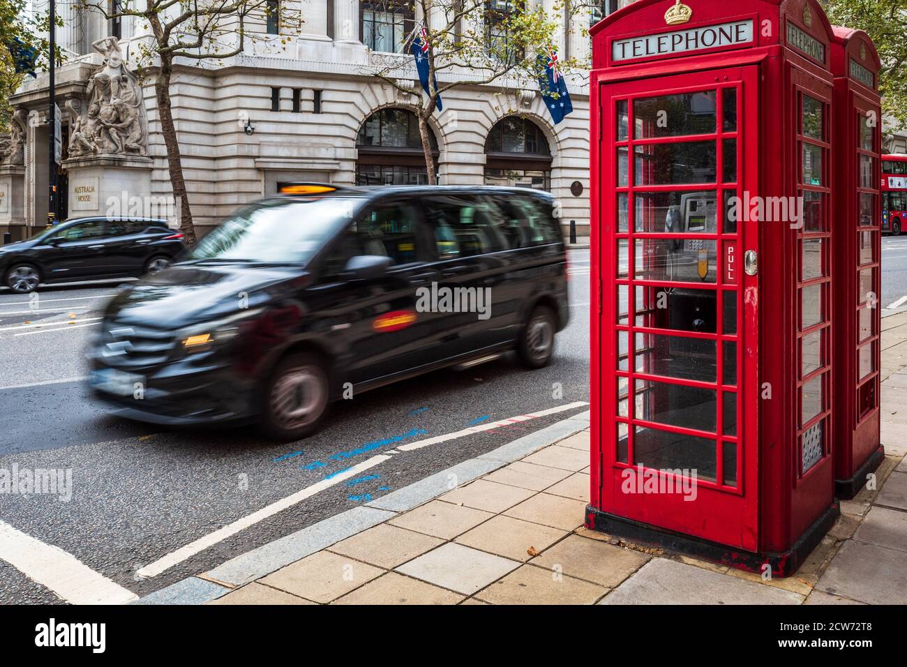 Iconic London - a Mercedes Vito London Taxi passes two traditional red telephone boxes in central London UK. Motion Blur of the taxi movement. Stock Photo