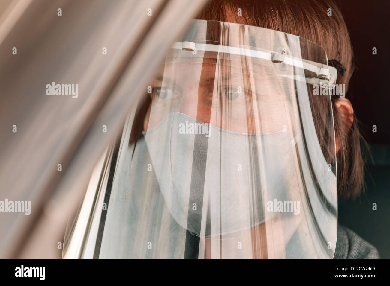 Female taxi driver with protective face mask and plastic visor waiting in car Stock Photo