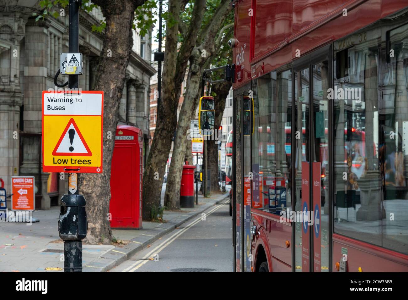 LONDON - SEPTEMBER 12, 2020: Low Trees warning sign with the side of a Red London Double Decker Bus passing and old telephone box and post box in the Stock Photo