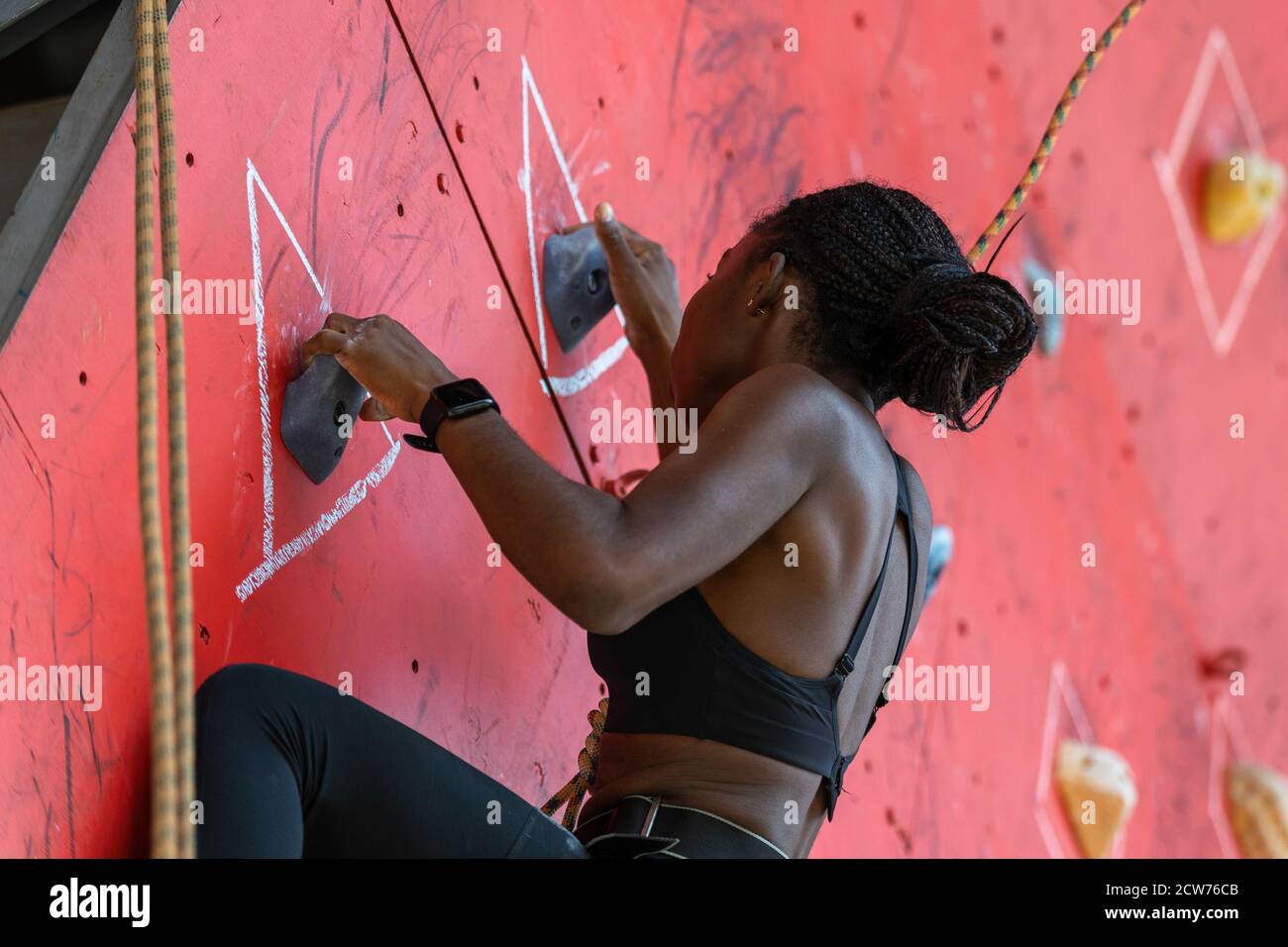 Young black woman climbing on training climbing wall. African climber girl  going through the route Stock Photo - Alamy