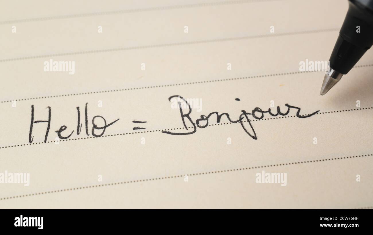 Beginner French language learner writing Hello word Bonjour for homework on a notebook macro shot Stock Photo