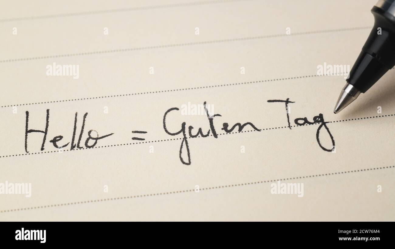 Beginner German language learner writing Hello formal word Guten Tag for homework on a notebook macro shot Stock Photo