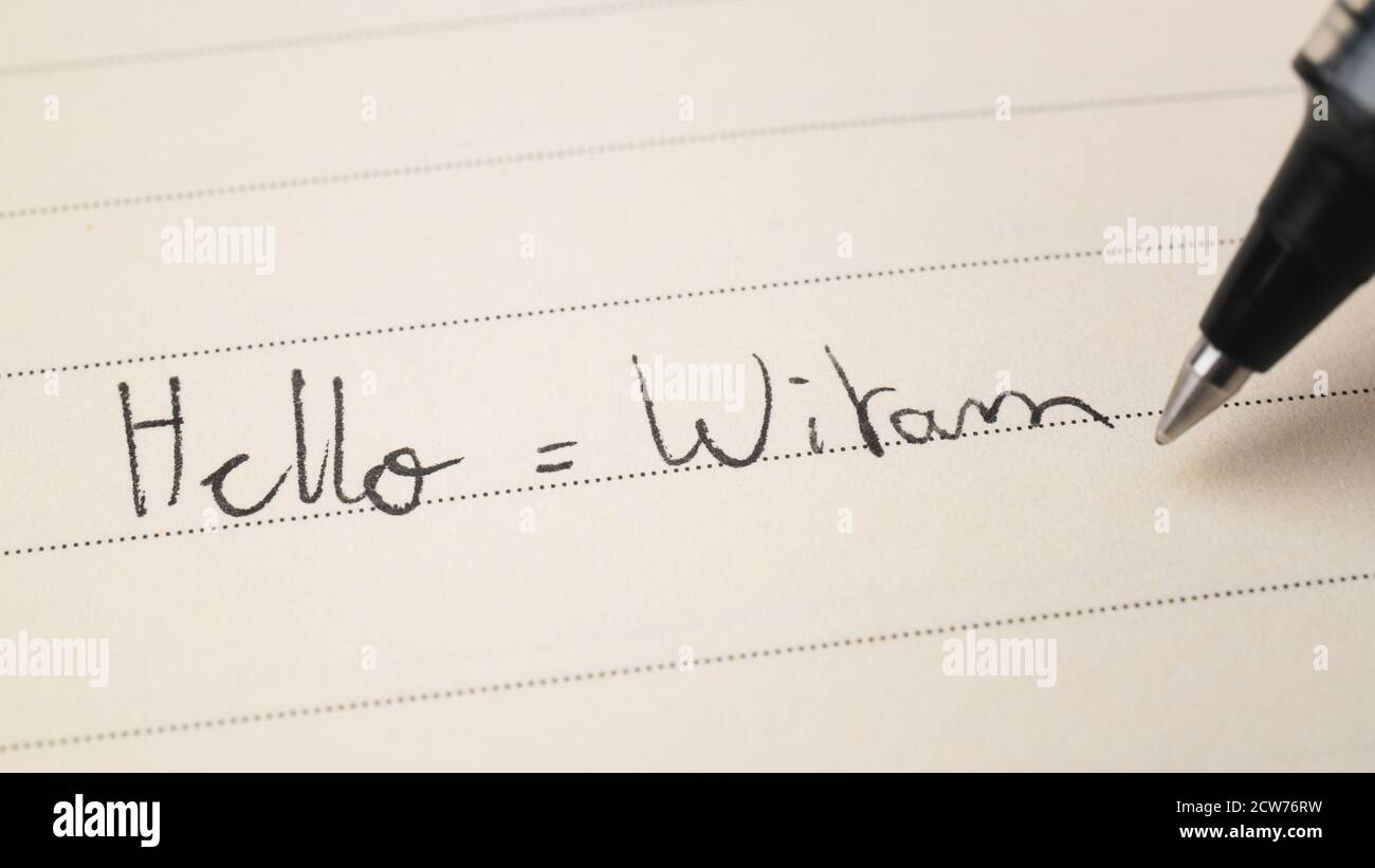 Beginner Polish language learner writing Hello word Witam for homework on a notebook macro shot Stock Photo