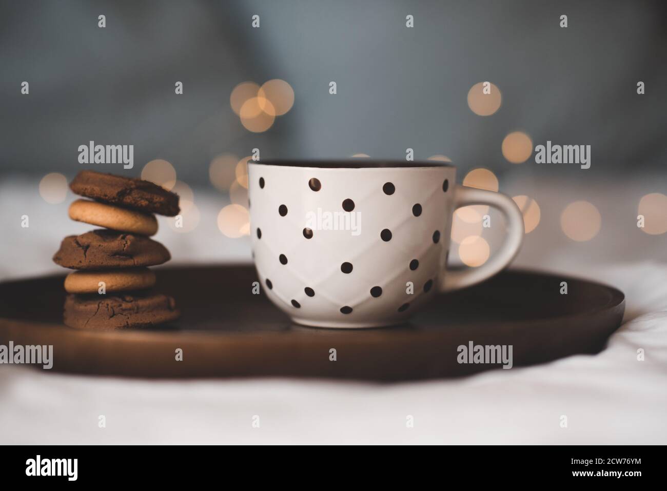 Cup of fresh hot tea with stack of chocolate cookies on wooden tray in bed close up. Good morning. Breakfast time. Focus on pastry. Stock Photo