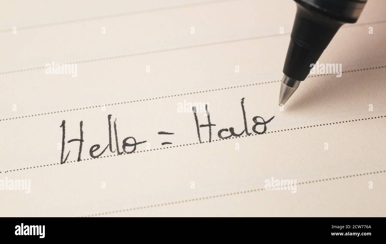 Beginner Indonesian language learner writing Hello word Halo for homework on a notebook macro shot Stock Photo