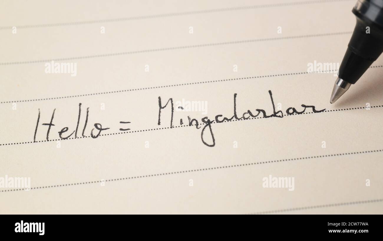 Beginner Burmese language learner writing Hello word Mingalarbar for homework on a notebook macro shot Stock Photo