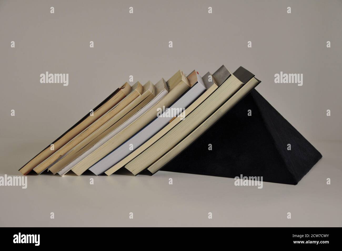 Books on shelf with blue felt pyramid support on white background side view Stock Photo