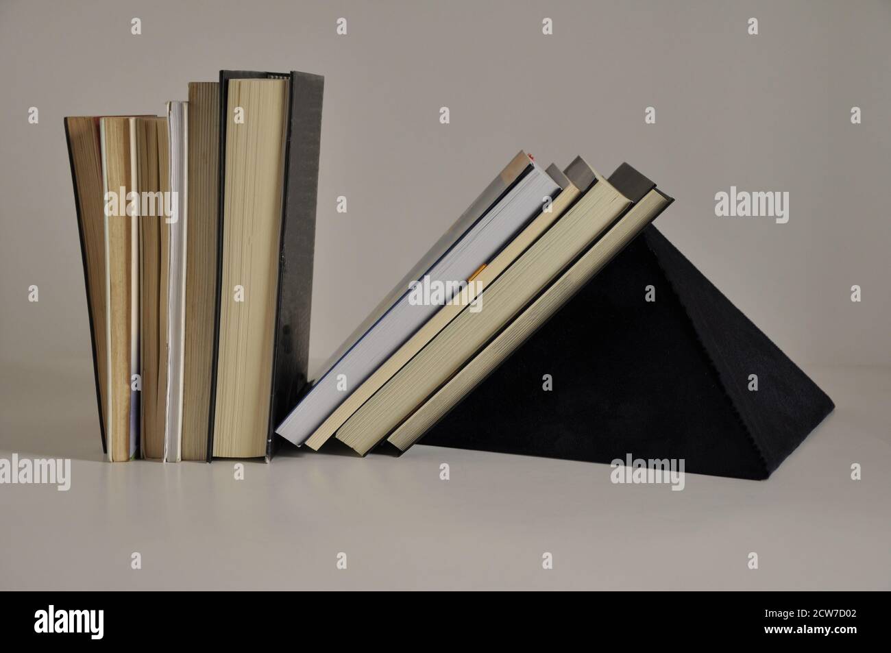 Books on shelf with blue felt pyramid support on white background side view, Brazil, South America Stock Photo