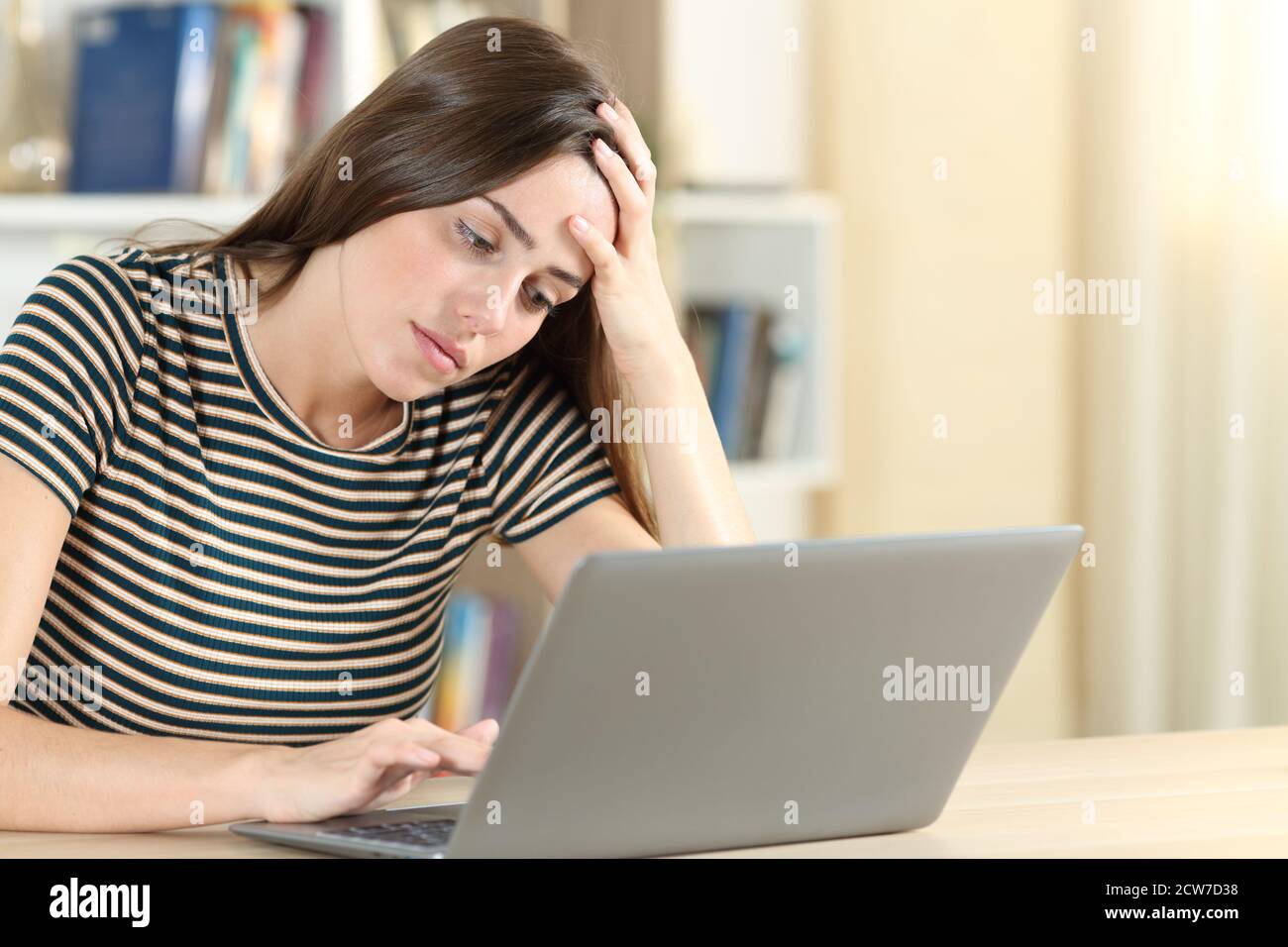 Tired teen using a laptop on a desk in the living room at home Stock Photo