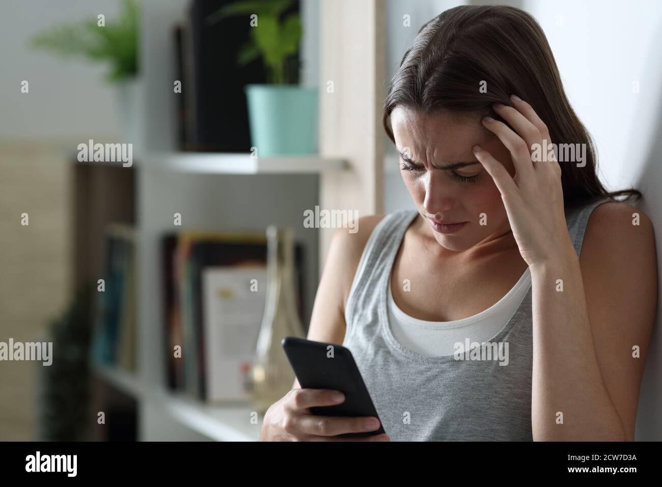 Sad teen checking smart phone content leaning in a wall at home in the night Stock Photo