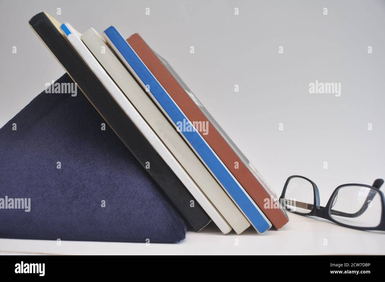 Books on shelf organized with support on blue felt pyramid white background side view Stock Photo