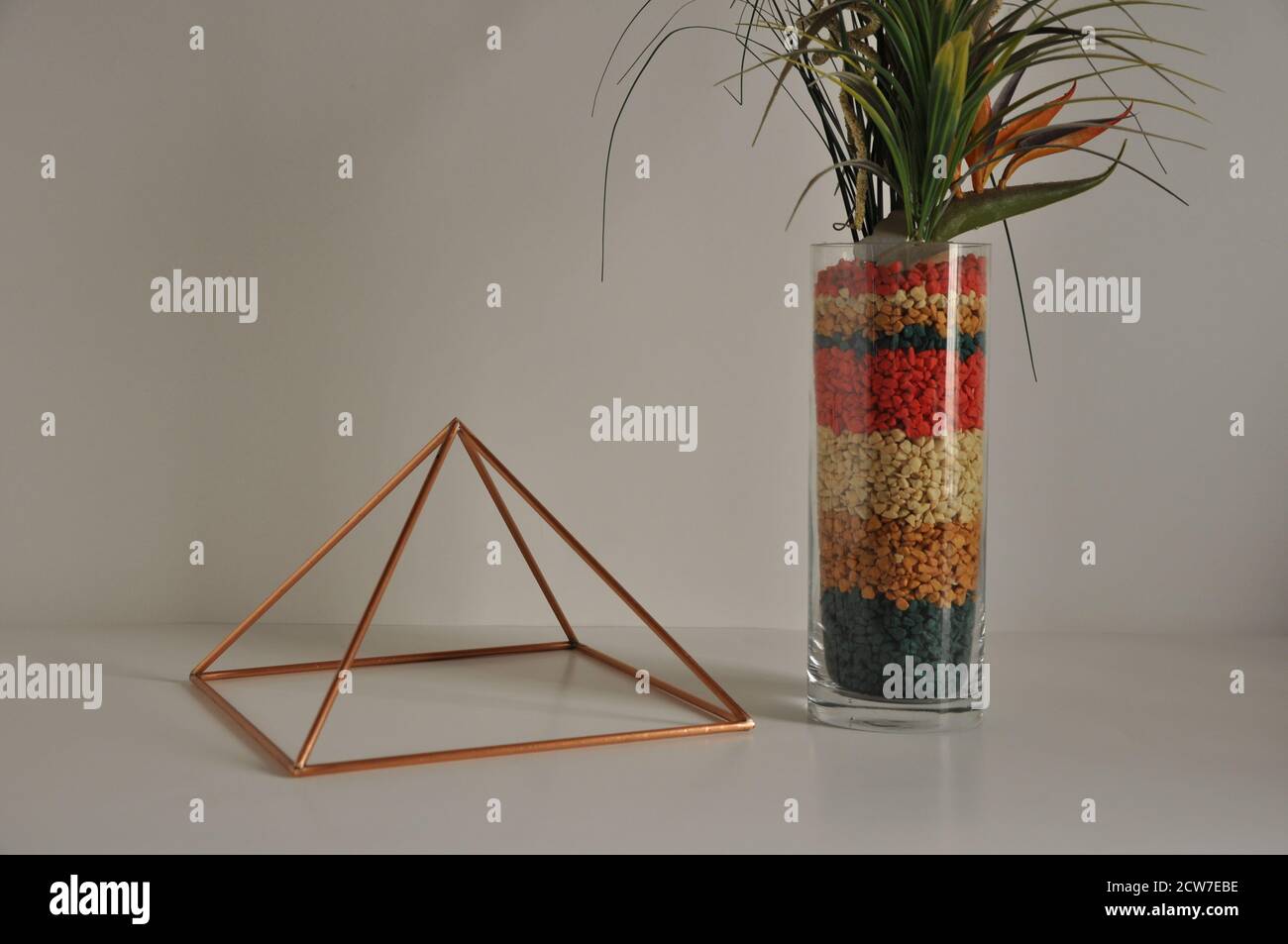 Pyramid Copper. pyramid with glass vase and decoration with unnatural flowers, with stones and multicolored flowers in base and white background. Stock Photo
