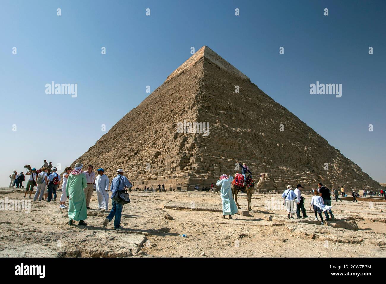 Visitors to the Giza plateau at Cairo in Egypt walk around the base of the Pyramid of Khafre. This pyramid still has a limestone cap at its peak. Stock Photo