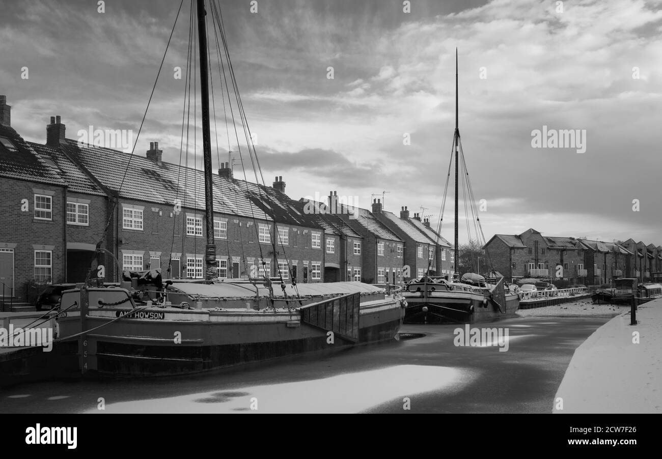 Vintage barges moored along the frozen beck (canal) and covered in snow flanked by town houses in Beverley, Yorkshire, UK. Stock Photo