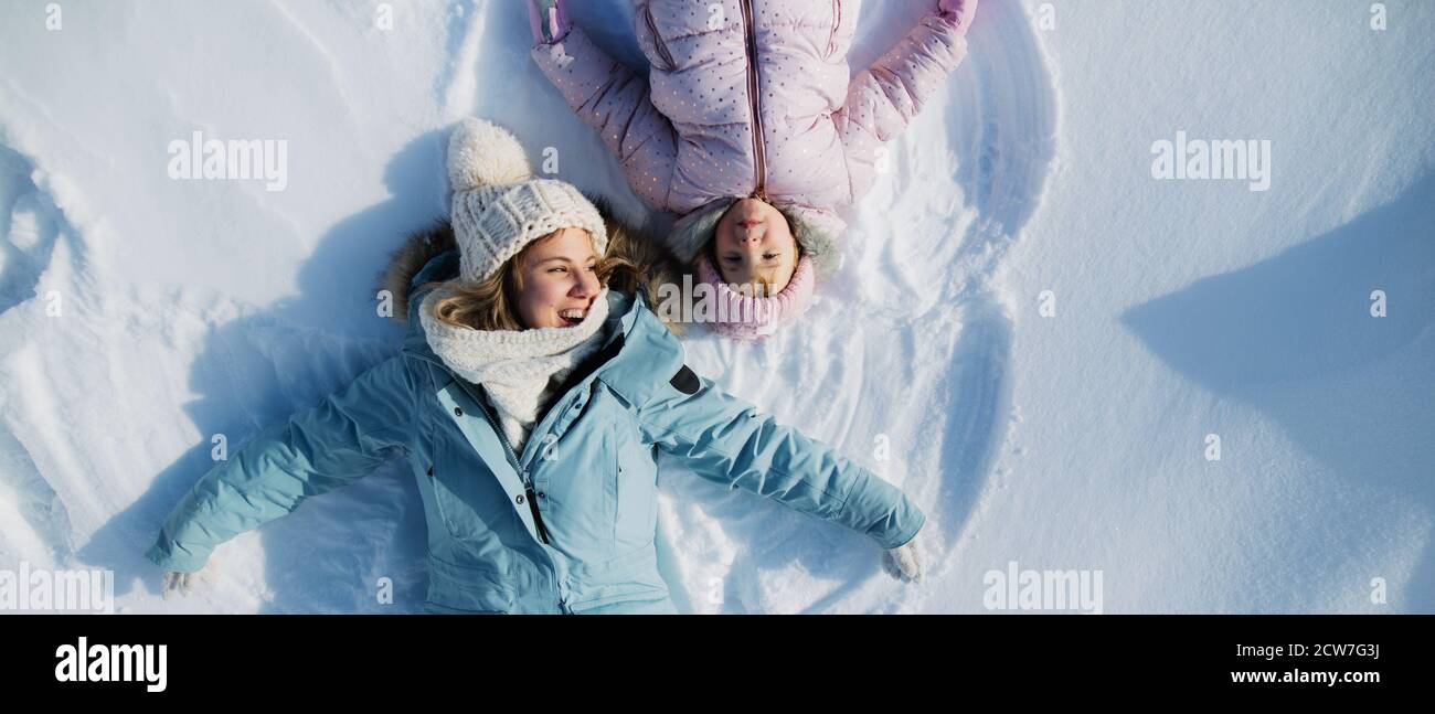 Top view portrait of cheerful mother with small daughter lying in snow in winter nature. Stock Photo