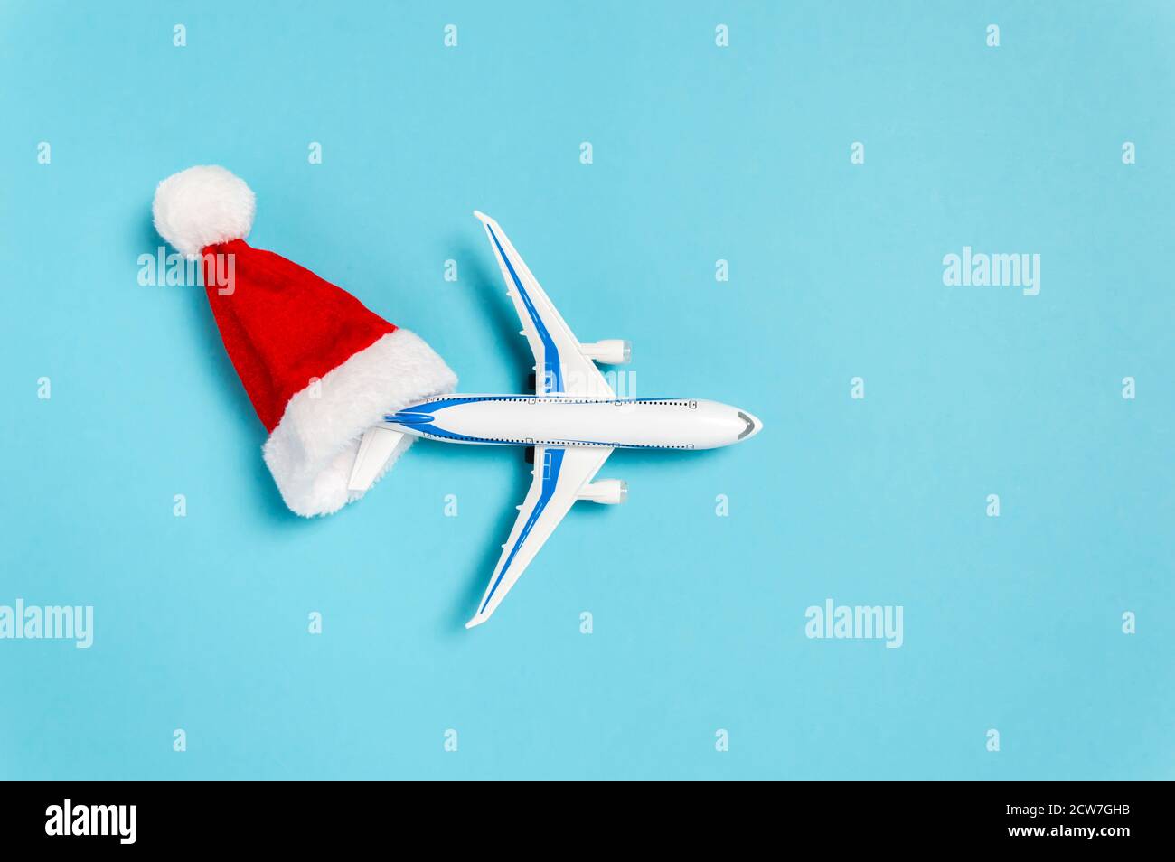 Christmas holidays travel concept. White airplane flying out of red Santa Clause hat on blue background. Flat lay style minimal composition for travel Stock Photo