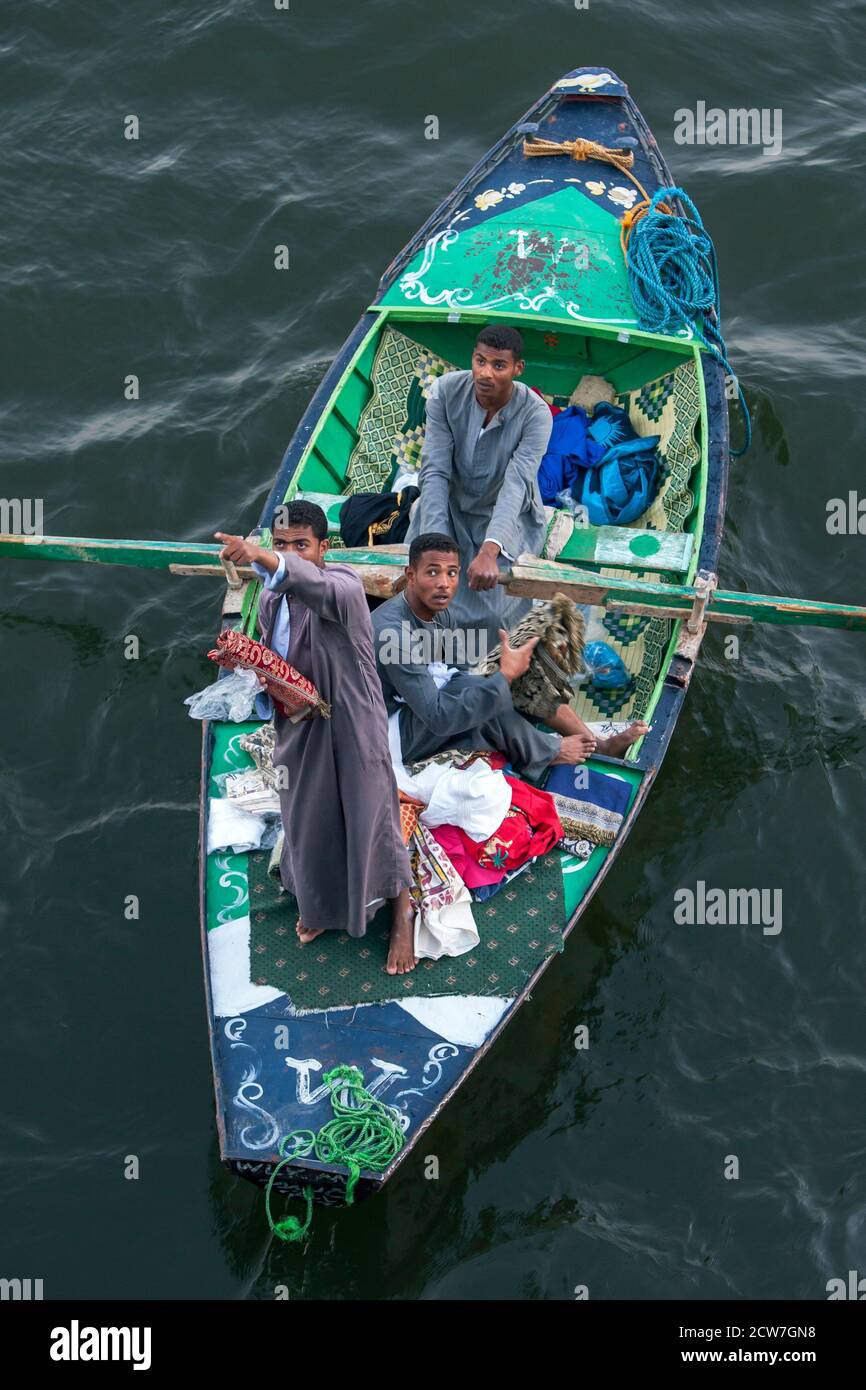 Salesmen in their rowing boat display their goods for sale to passengers aboard a floating hotel as it enters Esna Lock on the River Nile in Egypt. Stock Photo