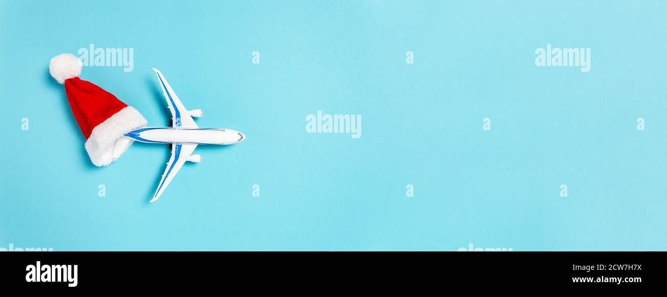 Christmas banner with holidays travel concept. White airplane flying out of red Santa Clause hat on blue background. Flat lay style minimal compositio Stock Photo