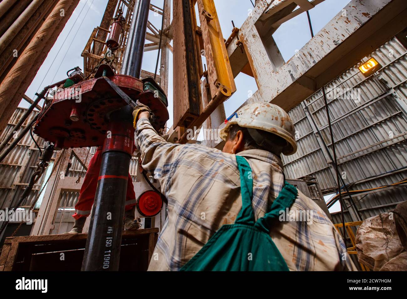 Drilling rig operations. Worker using electric clincher to connect drill pipes. Rear view. Zhaik