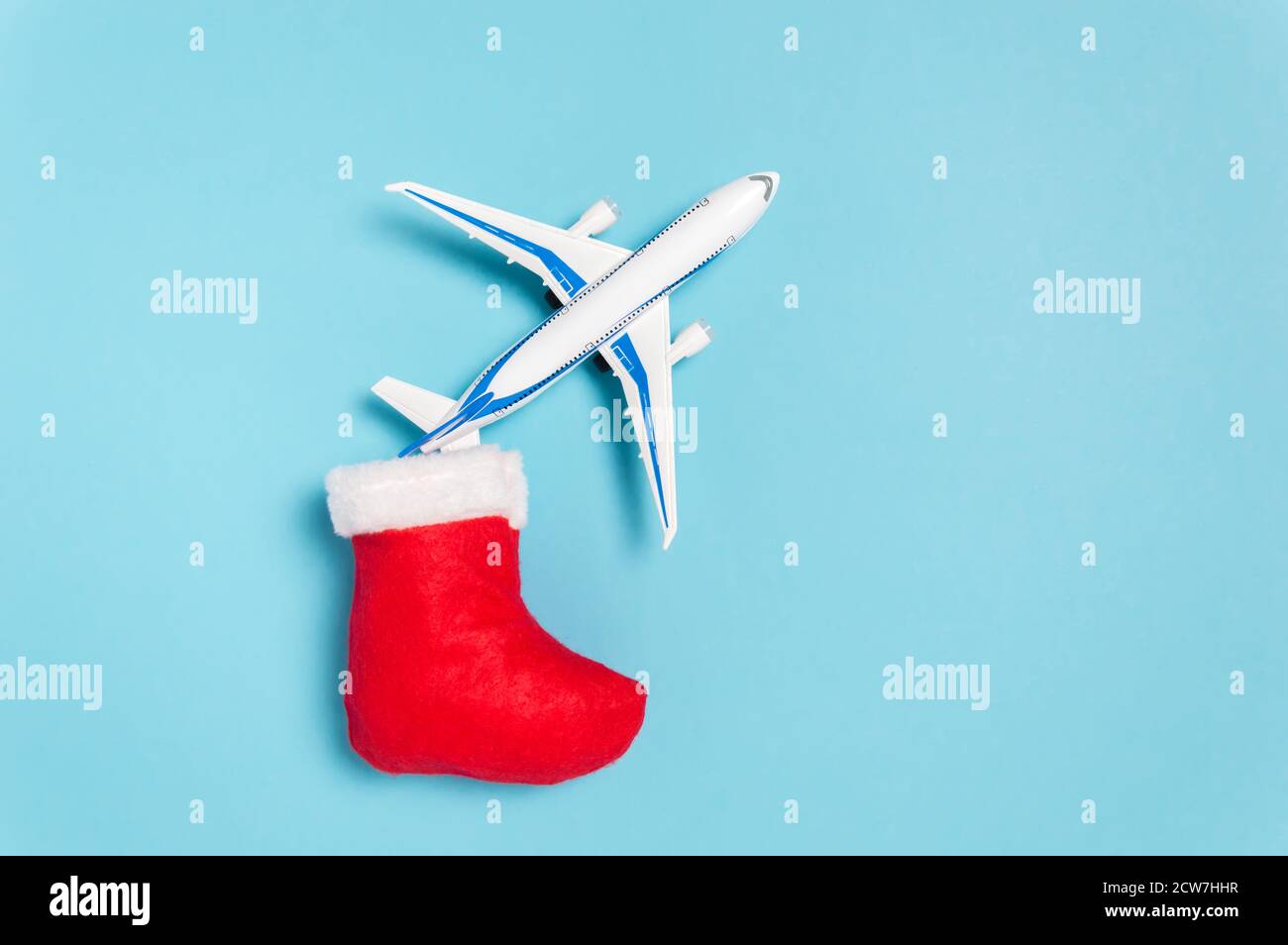 Christmas holidays travel concept. White airplane flying out of red Santa Clause sock on blue background. Flat lay style minimal composition for trave Stock Photo