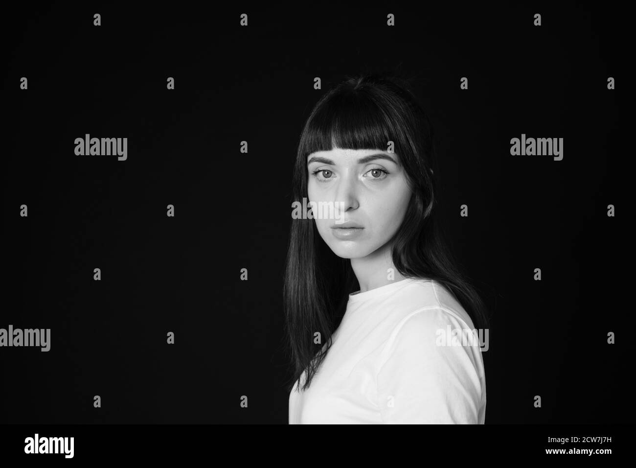 Sideview studio portrait of a pretty brunette woman in a white blank t-shirt, against a plain black background, looking at the camera Stock Photo