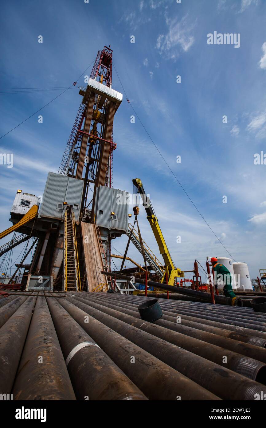 Zhaik-Munai oil deposit, Kazakhstan.Works on drilling rig. Rusted drilling pipes and oil worker on foreground. Blue sky and light clouds. Wide-angle Stock Photo