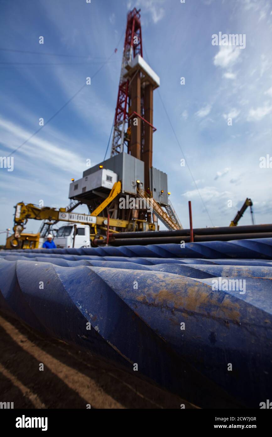 Oil deposit. Works on drilling rig. Blue rusted drilling pipes on front in focus.  Oil worker, truck crane and rig on foreground blurred. Blue sky Stock Photo