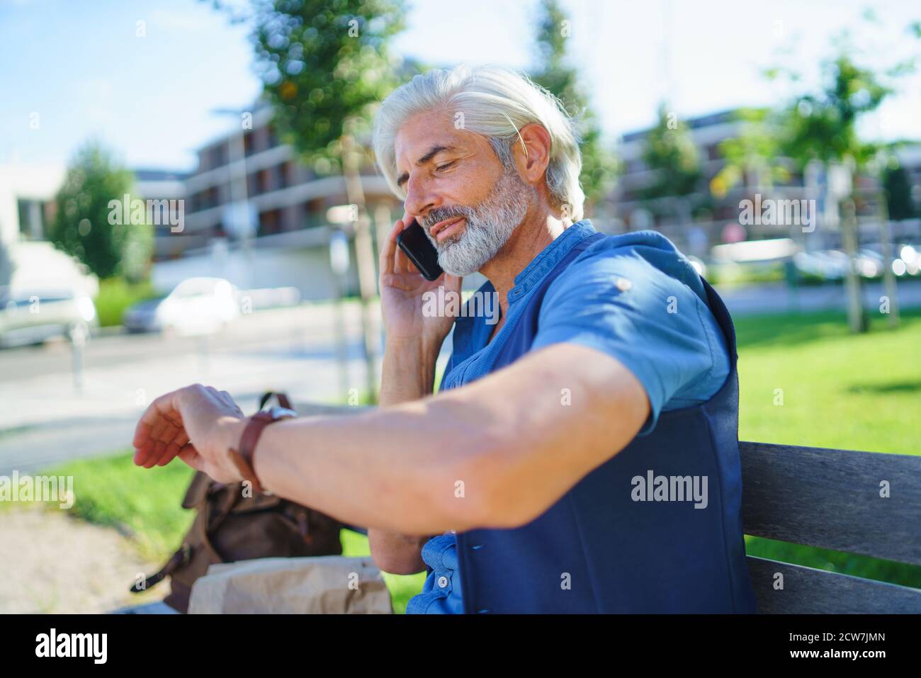 Portrait of mature man sitting outdoors in city, using smartphone. Stock Photo