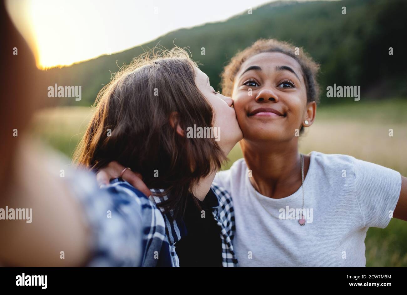 Front view of young teenager girls friends kissing outdoors in nature, taking selfie. Stock Photo
