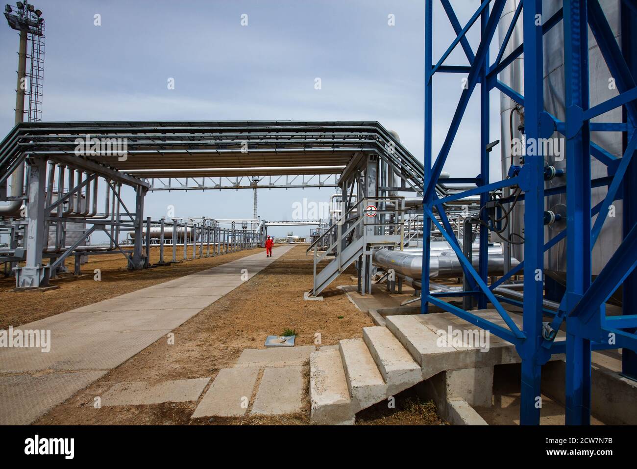 Oil refinery and gas processing plant. Pipelines and mast on grey sky. Refinery worker on background. Zhaik-Munai oil deposit, Kazakhstan. Stock Photo