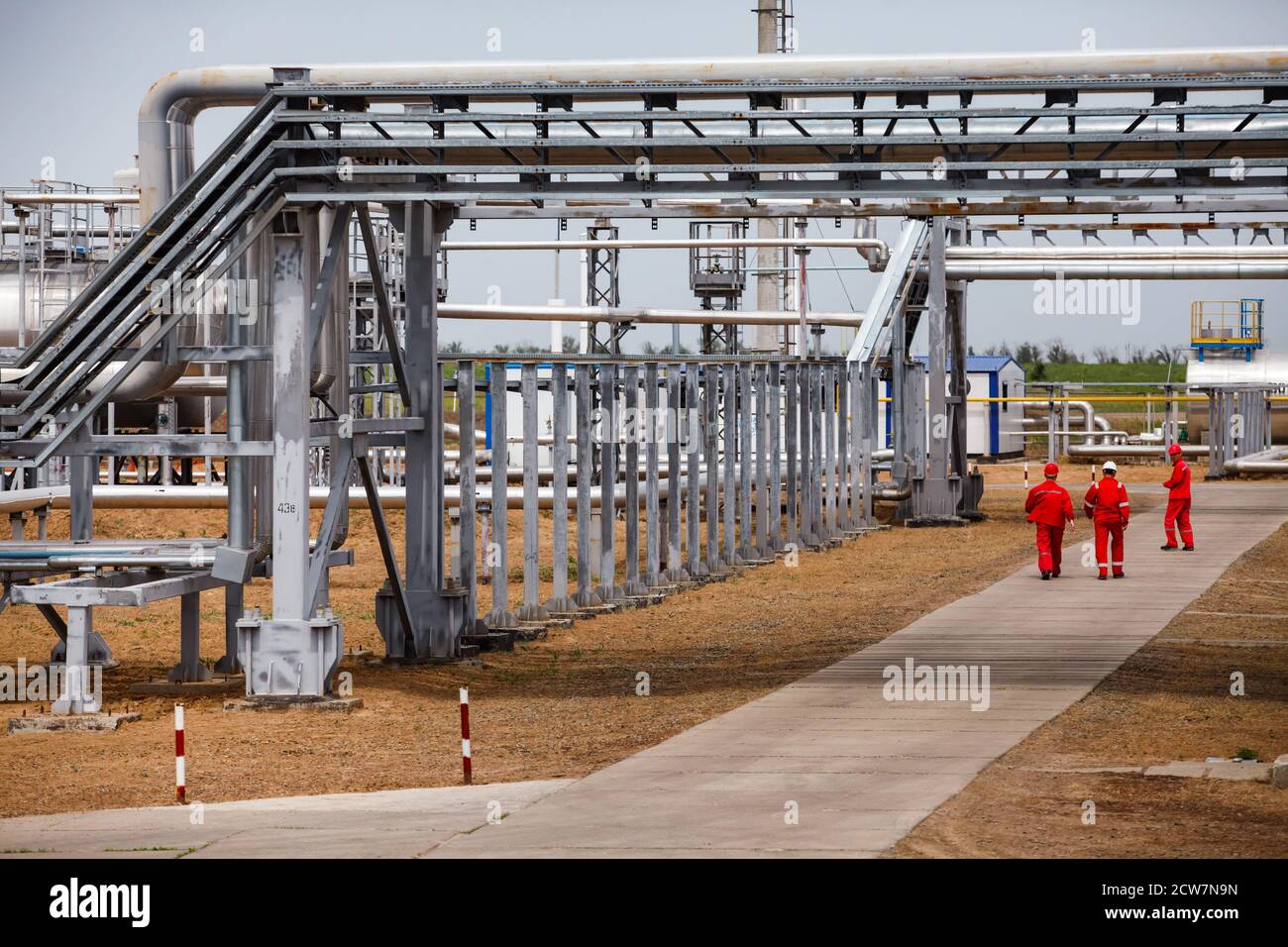 Oil refinery and gas processing plant. Three oil workers in red work wear and helmets under pipelines. Zhaik-Munai oil deposit, Kazakhstan. Stock Photo