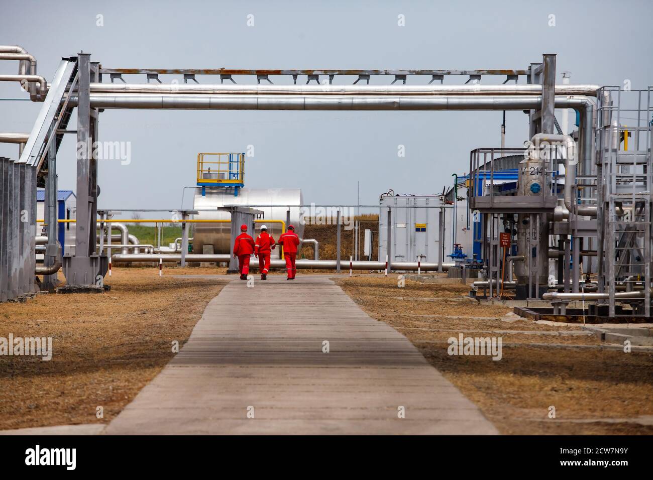 Three oil workers on oil refinery and gas processing plant under pipelines. Zhaik-Munai oil deposit, Kazakhstan. Stock Photo