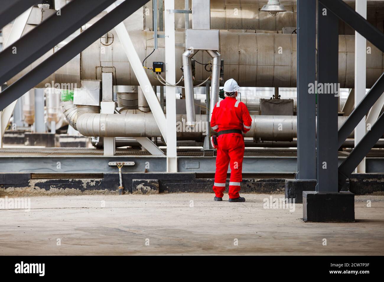 Engineer in white helmet & red work wear on metal pipe & tubes background. Oil refinery & gas processing plant. Zhaik-Munai oil deposit, Kazakhstan. Stock Photo