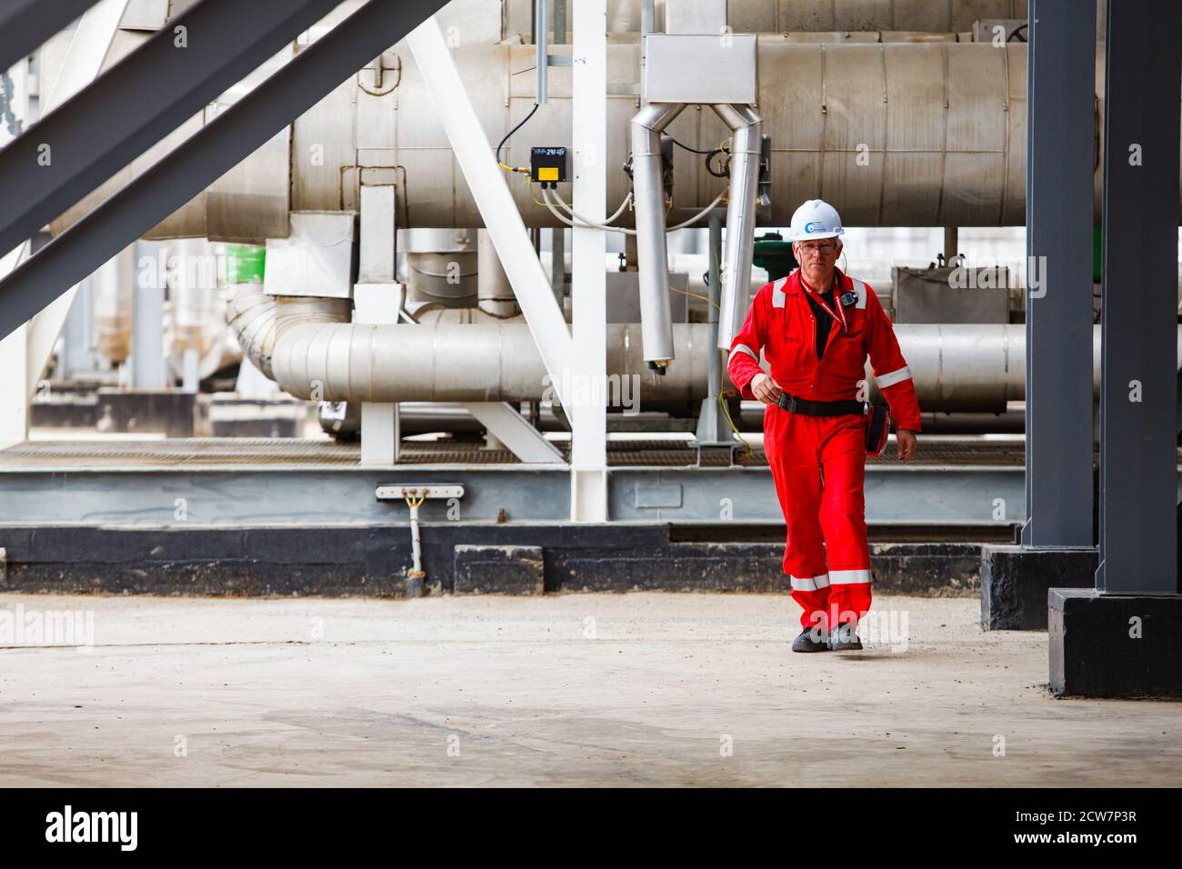 Engineer in white helmet & red work wear on metal pipe & tubes background. Oil refinery & gas processing plant. Zhaik-Munai oil deposit, Kazakhstan Stock Photo