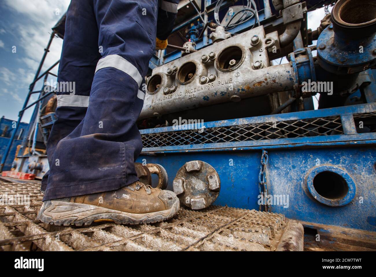Zhaik-Munai oil deposit, Kazakhstan. Maintenance worker fixing mud pump engine. Baker Hughes company.  Close-up of dirty working boots, no face. Stock Photo