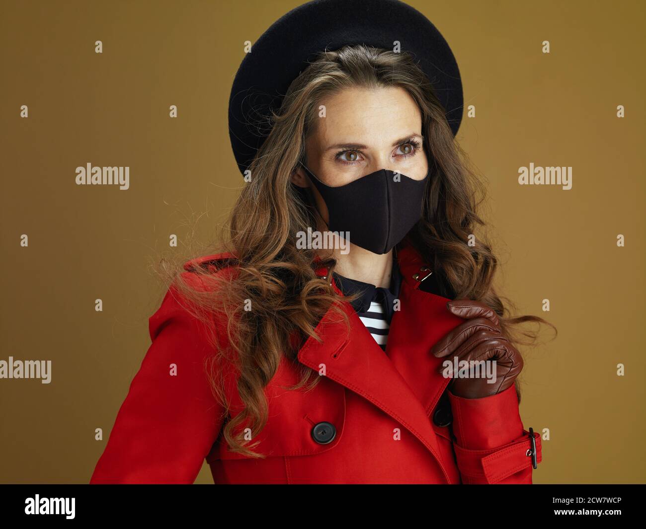 Life during covid-19 pandemic. elegant woman in red coat with black mask isolated on beige background. Stock Photo