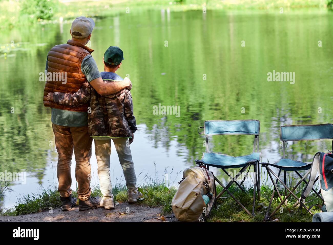Full length back view portrait of father and son standing by lake and enjoying nature during hiking or fishing trip, copy space Stock Photo