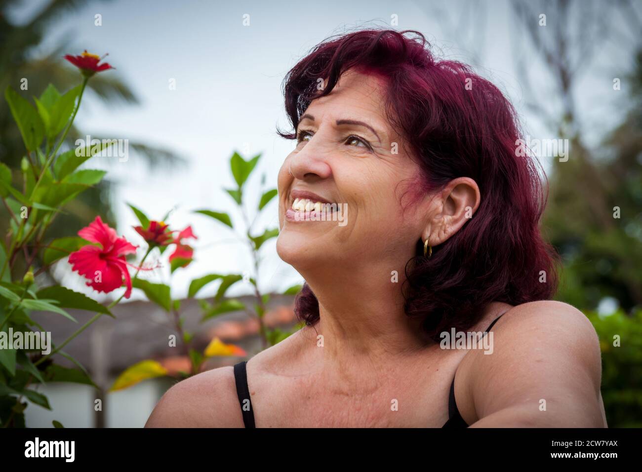 Portrait of a beautiful middle age latin woman outdoors in the garden with her hair just dyed in a redish color Stock Photo