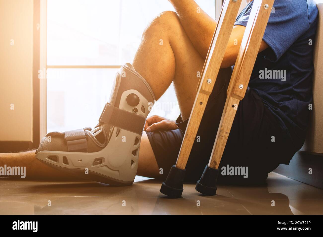 injured man broken ankle wearing ankle support sitting in the house with soft-focus and  over light in the background Stock Photo