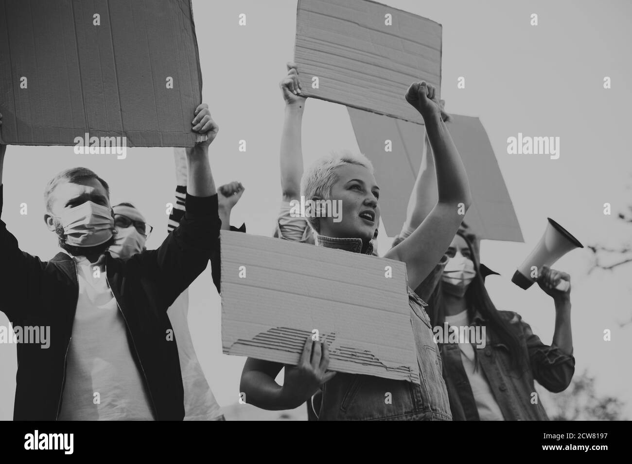 Black and white. Group of activists giving slogans in a rally. Caucasian men and women marching together in a protest in the city. Look angry, hopeful, confident. Blank banners for your design or ad. Stock Photo